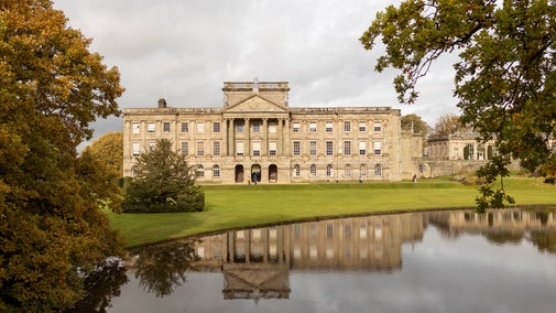 The exterior of the Georgian-style house at Lyme, Cheshire, in autumn, with the lake framed by orange and green foliage